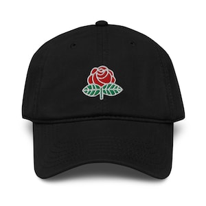 May include: A black baseball cap featuring an embroidered design on the front panel. The embroidery depicts a red rose with white outlines and two green leaves positioned at the base of the flower, centred on the crown of the hat.
