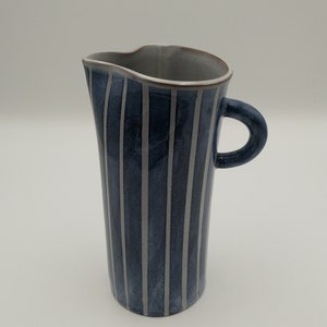 May include: A blue and white striped ceramic pitcher with a handle. The pitcher is tall and slender, with a slightly flared lip.