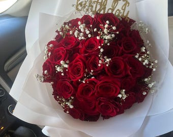 May include: A bouquet of red roses with white baby's breath and a gold glitter "happy birthday" topper.