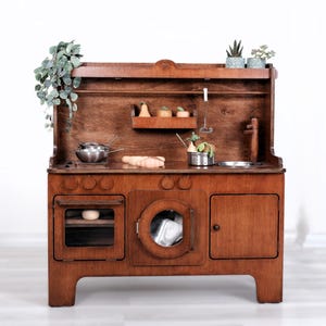 May include: A wooden toy kitchen with a dark brown finish. It features a stove top, oven, sink, and a washing machine. Accessories include a stainless steel pot, wooden utensils, and miniature plants. The kitchen is designed for children's play.