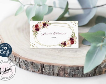 May include: A white place card with a gold geometric frame and burgundy and blush floral accents. The text "Jessica Anderson" and "Table 1" is printed on the card.