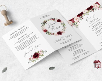 May include: A wedding invitation suite with a floral design. The front of the invitation features a wreath of burgundy and blush pink flowers with greenery. The text "Jessie and Richard" is written in a script font. The back of the invitation includes the wedding date, time, and location. The ceremony card lists the order of events for the wedding ceremony.