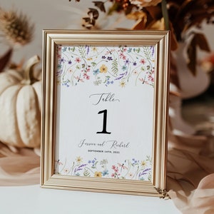 May include: Gold-framed table number card with a floral design and the text "Table 1 Jessica and Richard September 14th, 2021".