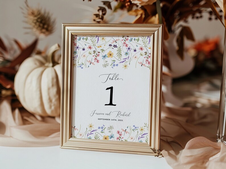 May include: Gold-framed table number card with a floral design and the text "Table 1 Jessica and Richard September 14th, 2021".