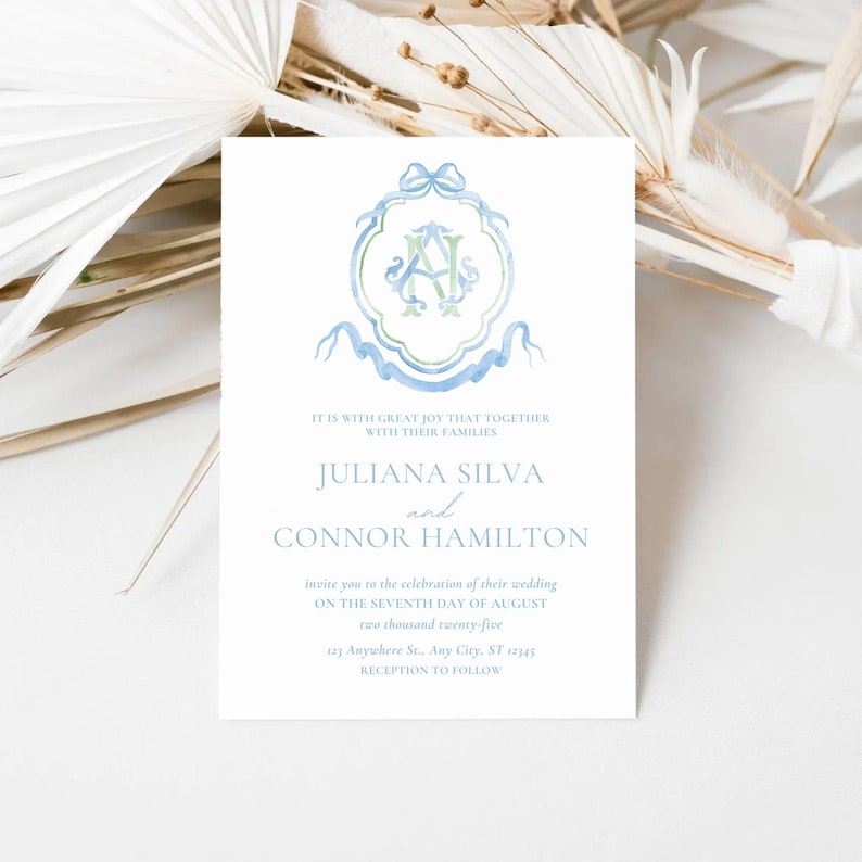 May include: A wedding invitation with a blue and green watercolor monogram. The invitation reads "It is with great joy that together with their families Juliana Silva and Connor Hamilton invite you to the celebration of their wedding on the seventh day of August two thousand twenty-five 123 Anywhere St. Any City, ST 12345 Reception to follow."