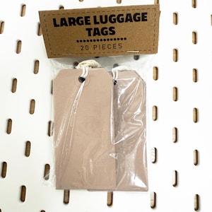 Peut inclure: Un paquet de grandes étiquettes à bagages de couleur marron clair, emballées dans un sac en plastique transparent. Le carton d'emballage porte l'inscription "LARGE LUGGAGE TAGS" et "20 PIECES".