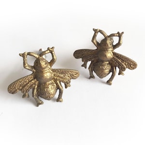May include: Two gold bee-shaped drawer pulls. The bees have raised details and are facing to the right.