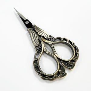May include: Antique gold-toned scissors with intricate floral designs and black handles. The scissors have a delicate, ornate look.