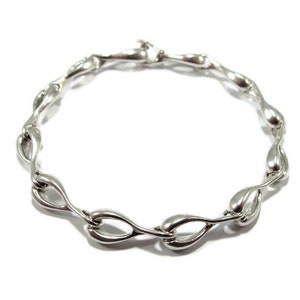 May include: A silver bracelet featuring a distinctive twisted and linked design. The bracelet is crafted from smooth, rounded links that are joined together in a continuous loop.