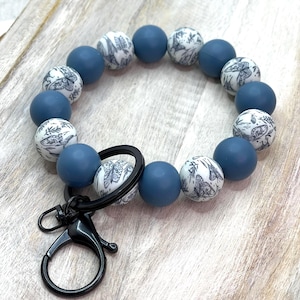May include: A blue beaded keychain wristlet with a black clasp. The wristlet features alternating solid blue and white beads with a black and white botanical pattern.