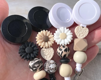 May include: Three black and white retractable badge reels with beaded charms. The charms include black and white animal print beads, beige and brown heart and flower beads, and a beige and brown geometric bead.
