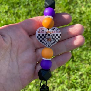 Pu&ograve; includere: Un portachiavi con perline a tema Halloween con chiusura nera. Il portachiavi presenta perline geometriche nere, perline rotonde viola e arancioni e un ciondolo a forma di cuore con un fantasma che legge un libro e la scritta "READ MORE BOOKS".