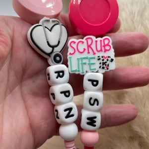 Peut inclure: Deux porte-badges rétractables roses avec des perles blanches qui épellent "RN" et "PSW". Les porte-badges ont un cœur rose avec un charme stéthoscope et un charme blanc qui dit "Scrub Life" avec un motif léopard rose et noir.