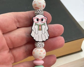 Op de afbeelding: Een kralen lanyard met een witte spookbedel met een roze bril en een boek. De lanyard heeft roze, wit bloemige en mintgroene kralen, met een zilveren sluiting.