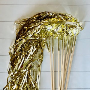 May include: A bundle of gold streamer wands with wooden sticks. The streamers are made of shiny gold foil and are ready to be used for a party or celebration.