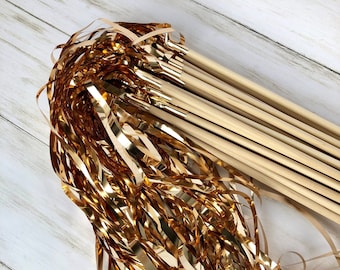 May include: A bundle of gold metallic streamer wands with wooden sticks. The streamers are long and flowing, creating a festive and celebratory look.