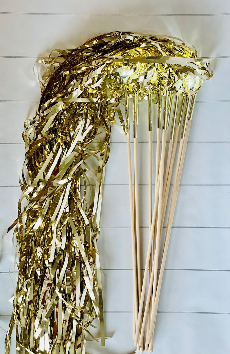 May include: A bundle of gold streamer wands with wooden sticks. The streamers are made of shiny gold foil and are ready to be used for a party or celebration.