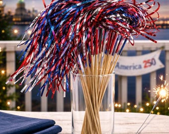 May include: A clear glass vase filled with wooden skewers topped with red, white, and blue metallic streamers. The background features fireworks, the Statue of Liberty, and a banner that reads "America 250."