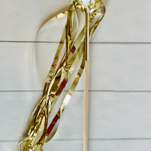 May include: A gold streamer wand with a clear plastic ball at the top. The wand is made of wood and has a gold ribbon attached to the ball.