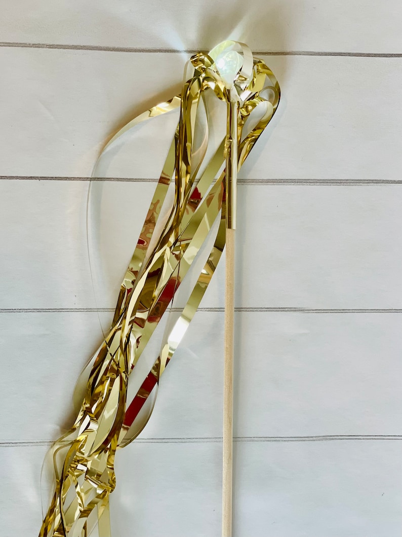 May include: A gold streamer wand with a clear plastic ball at the top. The wand is made of wood and has a gold ribbon attached to the ball.