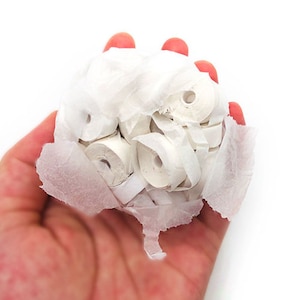 May include: A hand holding a collection of small, white paper rolls. The rolls are tightly packed together and wrapped in thin, white paper. The background is plain white.