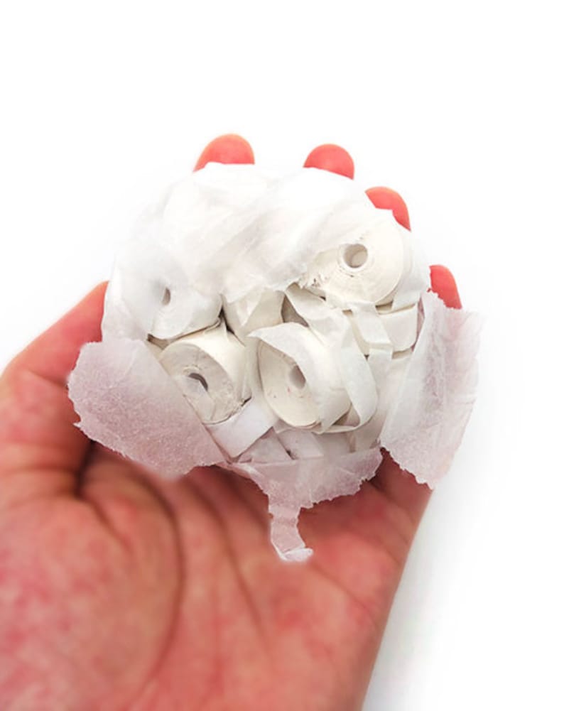 May include: A hand holding a collection of small, white paper rolls. The rolls are tightly packed together and wrapped in thin, white paper. The background is plain white.