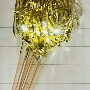 May include: A bunch of gold streamer wands with wooden sticks. The streamers are curled and twisted, creating a festive and celebratory look.