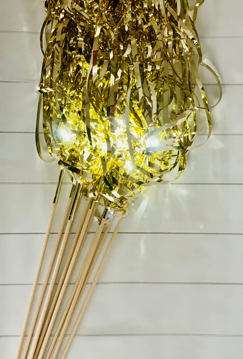 May include: A bunch of gold streamer wands with wooden sticks. The streamers are curled and twisted, creating a festive and celebratory look.