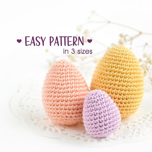 May include: Three crocheted Easter eggs in different sizes. The largest egg is yellow, the middle egg is peach, and the smallest egg is purple.