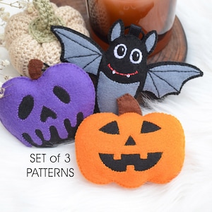 May include: Set of three Halloween-themed felt ornaments. Includes a purple skull pumpkin, an orange jack-o'-lantern, and a black bat with gray wings. The text "SET of 3 PATTERNS" is visible.