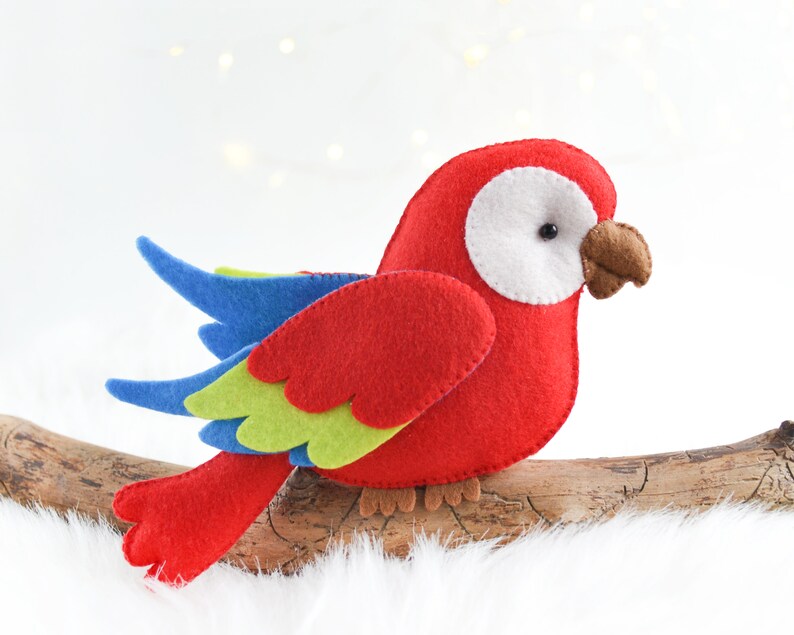 May include: A red, blue, and green felt parrot with a white eye perched on a branch.