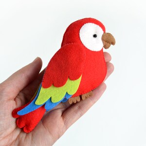 May include: A red felt parrot with green, blue, and brown accents. The parrot has a white eye and a brown beak.