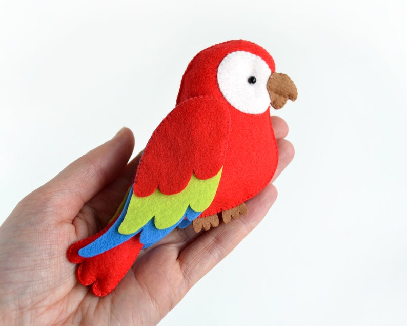 May include: A red felt parrot with green, blue, and brown accents. The parrot has a white eye and a brown beak.