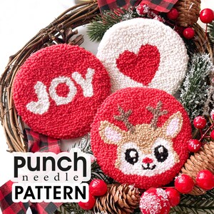 Op de afbeelding: Drie rode en witte punch needle-versieringen met kerstthema's. De versieringen tonen een rendier, een hart en het woord "JOY".
