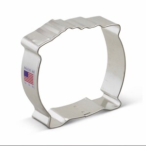 May include: A silver metal cookie cutter shaped like a large, rounded rectangle with a wavy top edge. The cutter has a small, rectangular handle on the bottom and says "MADE IN USA" on the side.