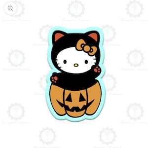 May include: A Halloween-themed cookie cutter featuring a cartoon cat character dressed in a black costume with a bow, sitting inside a carved orange pumpkin. The cutter has a light blue outline.