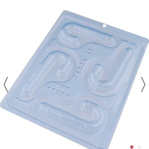 K&ouml;nnte beinhalten: Eine transparente Plastik-Bonbonform mit sechs Hohlr&auml;umen in Form von Zuckerstangen. Die Form ist hellblau und hat den Text "64564 13 9" aufgedruckt.