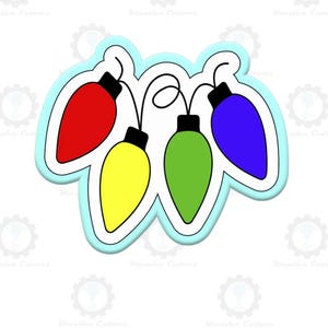 Op de afbeelding: Een kleurrijke koekjesvorm in de vorm van vier kerstverlichting. De lampjes zijn rood, geel, groen en blauw, elk met een zwarte dop. De vorm heeft een lichtblauwe omtrek.