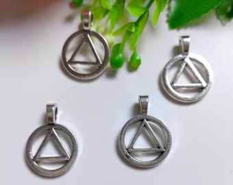 Puede incluir: Cuatro colgantes de metal en tono plateado, cada uno con un marco circular exterior que encierra un triángulo centrado. Cada colgante incluye una pequeña anilla en la parte superior para su sujeción, con un acabado metálico liso y brillante.