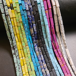 May include: Assortment of colorful rectangular gemstone beads, including turquoise, blue, green, yellow, white, and purple. The beads are arranged in rows, creating a vibrant and colorful display.