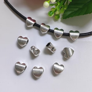 Puede incluir: Un conjunto de cuentas de corazón plateadas con un dije de calavera. Las cuentas están enhebradas en un cordón negro.