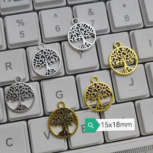 Puede incluir: Seis abalorios de árbol de la vida en plata y oro sobre un teclado blanco. Los abalorios miden 15x18mm.