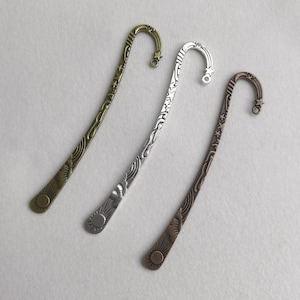 Puede incluir: Tres marcadores de metal en tonos bronce, plata y cobre. Cada marcador tiene una parte superior curva con un diseño de estrella y un tallo decorativo con patrones de sol y olas. Ideal para los lectores.