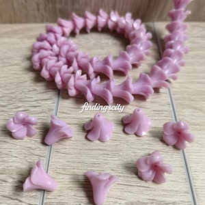 May include: A light purple flower-shaped bead strand and several loose light purple flower beads. The text C# Light Purple and findingscity are visible. Each bead features a five-petal design with a central hole for stringing, crafted from a smooth, solid-colored material.