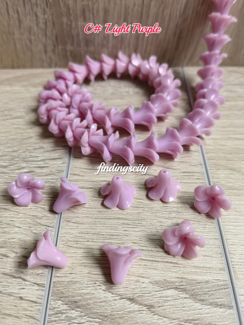 May include: A light purple flower-shaped bead strand and several loose light purple flower beads. The text C# Light Purple and findingscity are visible. Each bead features a five-petal design with a central hole for stringing, crafted from a smooth, solid-colored material.