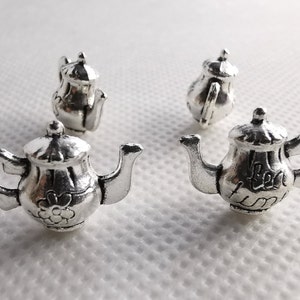 Könnte beinhalten: Vier silberne Teekannen mit aufwendigen Designs. Die Teekannen sind klein und haben einen Vintage-Look.