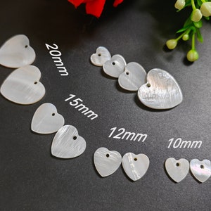 May include: Assortment of white mother of pearl heart-shaped embellishments in various sizes: 20mm, 15mm, 12mm, and 10mm. Each heart has a small hole at the top.