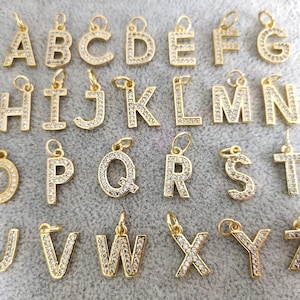 May include: A set of 26 gold-tone alphabet letter charms, each letter is encrusted with clear rhinestones. The charms are arranged in alphabetical order.