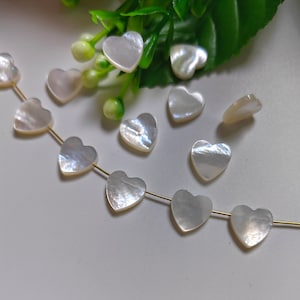 May include: A strand of white heart-shaped shell beads on a gold chain. The beads are strung together with a knot between each bead. The beads are scattered around the chain.