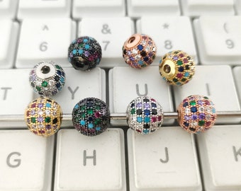 May include: Eight round beads with a variety of colorful gemstones and clear rhinestones. The beads are arranged on a keyboard with a silver metal rod running through them.